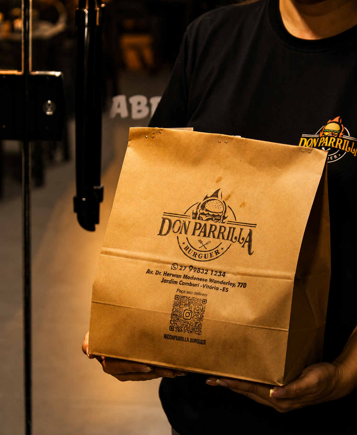 Atendente do Don Parrilla Burguer segurando sacola de delivery personalizada da marca